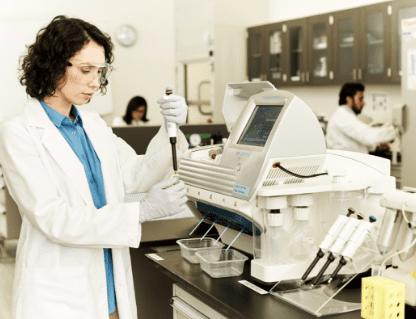 A woman in lab coat and gloves working on a device.